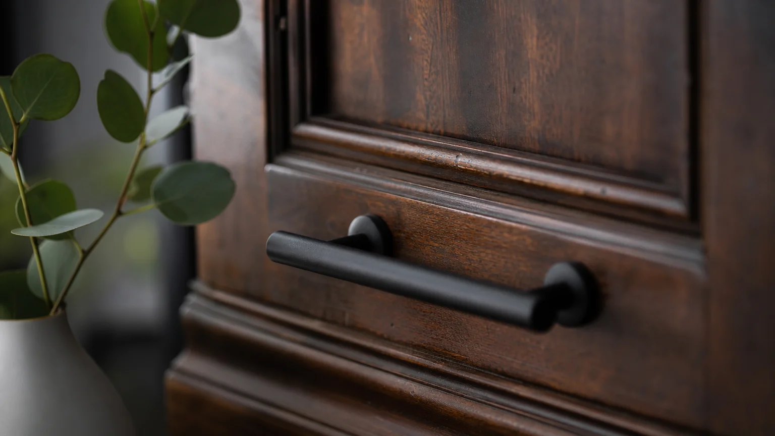 A close-up shot of dark vintage wood grain paired with a modern black handle and a green eucalyptus leaf.